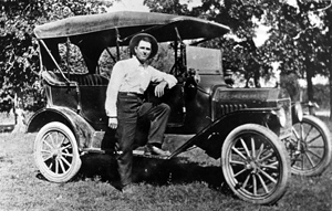 Man standing next to old model car in grassy field